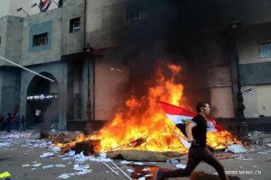 An Egyptian protester runs past a burning site near the headquarters of Muslim Brotherhood in Alexandria on June 28, 2013.